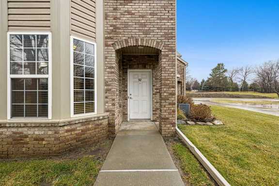 Brick apartment townhome exterior with covered arched entry, private front door, and landscaped lawn.