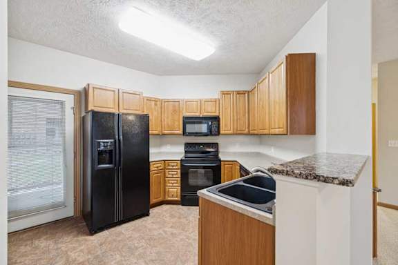 Kitchen with natural wood cabinets, black appliances, double-basin sink, laminate countertops, and vinyl tile flooring.