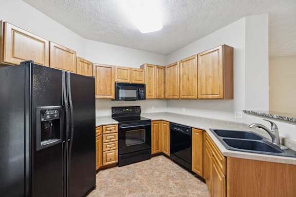 Corner kitchen layout featuring upper and lower cabinetry, black refrigerator, electric range with microwave, and dishwasher.