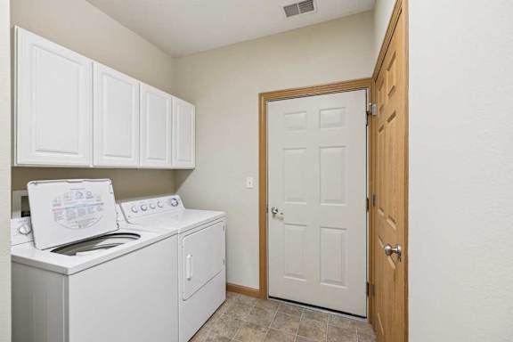 Laundry room with full-size washer and dryer, upper storage cabinets, and tile-look flooring.