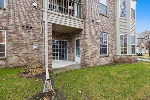 Brick apartment exterior with ground-level patio, sliding glass door entry, and upper balcony.