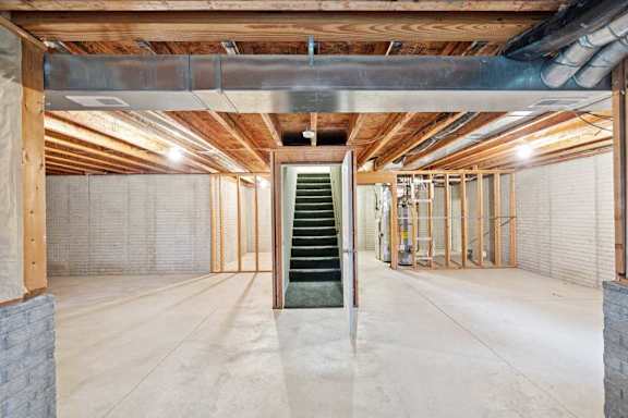 Unfinished duplex basement with exposed ceiling joists, concrete floors, utility area, and staircase access to main level.