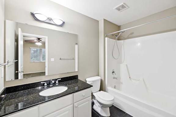 Full bathroom with single-sink vanity, granite countertop, toilet, and tub and shower combination.