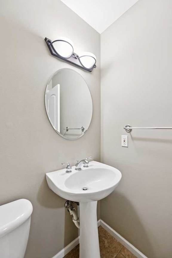 Half bathroom with pedestal sink, oval mirror, and wall-mounted lighting.