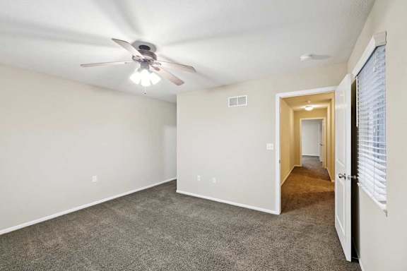 Spacious bedroom with plush carpet, ceiling fan, and hallway access.
