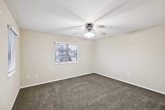 Large bedroom with neutral carpet, ceiling fan, and single window for natural light.