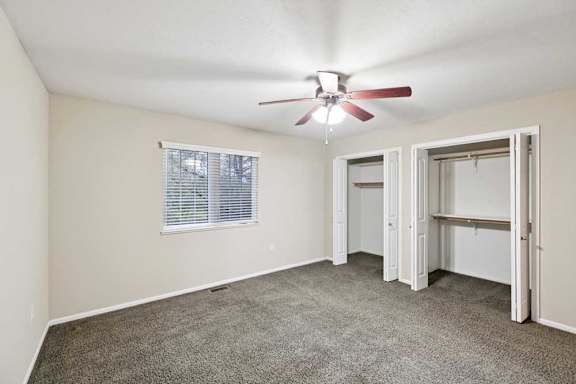 Primary bedroom with ceiling fan, wide window, and dual closets with built-in shelving.