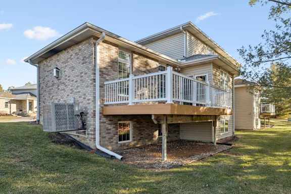 Reard duplex exterior with elevated deck, white railing, brick and siding facade, and backyard lawn.