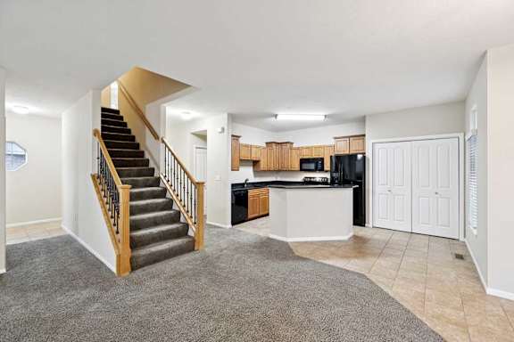 Open-concept living space with staircase, carpet and tile flooring, and kitchen with peninsula seating.