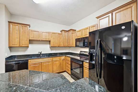 Kitchen with natural wood cabinets, black appliances, granite countertops, and peninsula with bar seating.