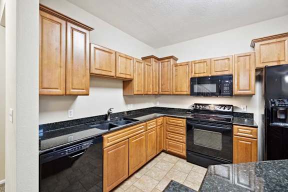 L-shaped kitchen featuring black dishwasher, electric range with microwave, double-basin sink, and tile flooring.