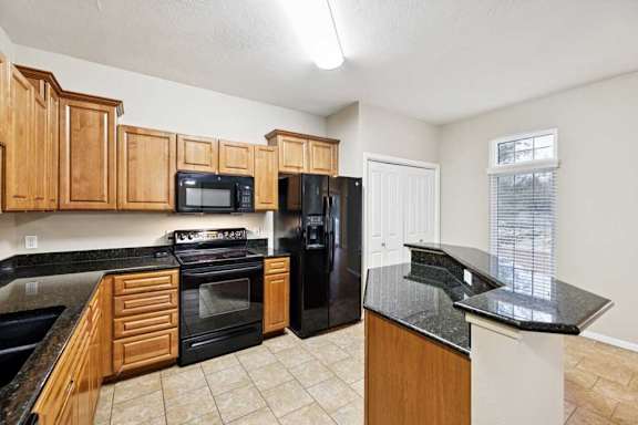 Kitchen with granite peninsula, black refrigerator, pantry closet, and adjacent dining area with large window.