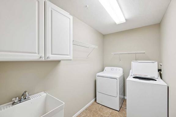 Laundry room with utility sink, washer and dryer, upper cabinets, and wire shelving.