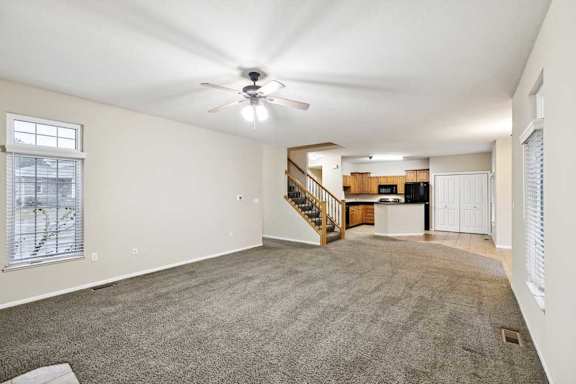 Large living room with multiple windows, neutral carpet, and open layout to kitchen and dining area.