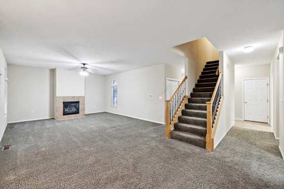 Open living space featuring staircase, fireplace, and wide carpeted area for flexible furniture layout.