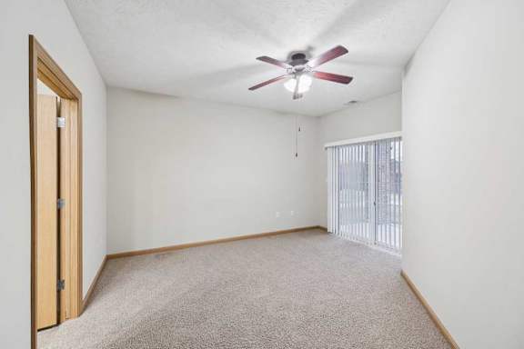 Spacious bedroom with plush carpet, ceiling fan, and sliding glass door to private balcony or patio.