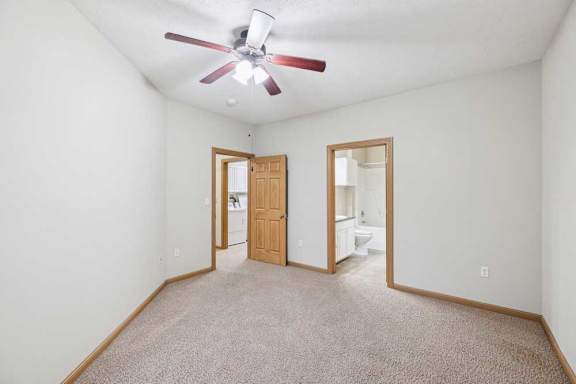 Primary bedroom with neutral walls, ceiling fan, and en-suite bath and laundry access.