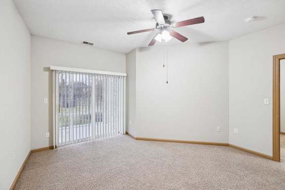Bright bedroom with large window, ceiling fan, and soft neutral finishes.
