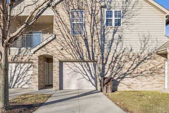 Townhome-style exterior with attached garage, balcony above, and brick and siding façade.