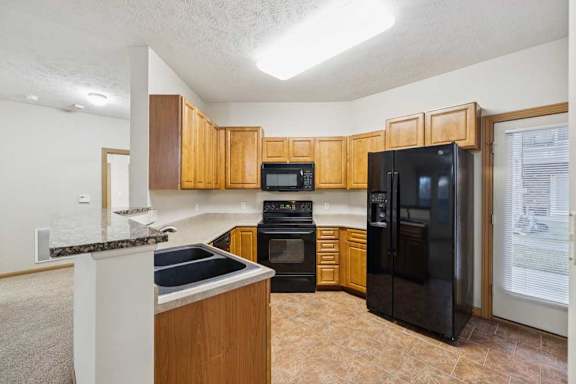 Kitchen with natural wood cabinets, black appliances, double-basin sink, and door to private balcony.