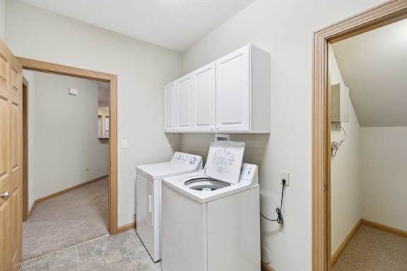 Laundry area with overhead cabinetry, adjacent utility closet, and doorway to carpeted living space.