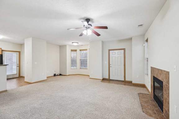 Spacious open living room with plush carpet, ceiling fan, tiled entry, and corner gas fireplace.