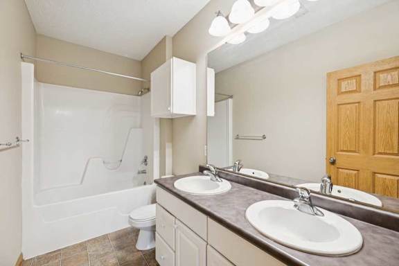 Full bathroom with double-sink vanity, large mirror, tub and shower combination, and overhead vanity lighting.