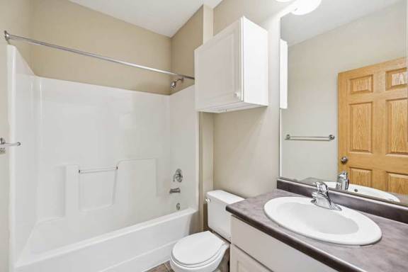 Apartment bathroom with tub and shower combination, single-sink vanity, wall cabinet, and wood trim accents.