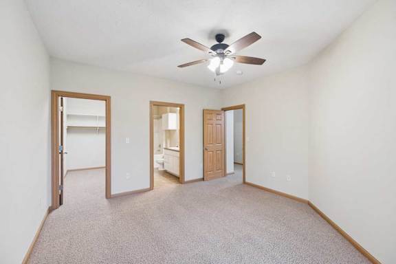 Spacious bedroom with neutral carpet, ceiling fan, and wood trim, featuring an en-suite bathroom and large walk-in closet through separate doorways.