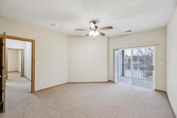 Spacious bedroom with neutral carpet, ceiling fan, and sliding glass door leading to a private balcony with outdoor views.