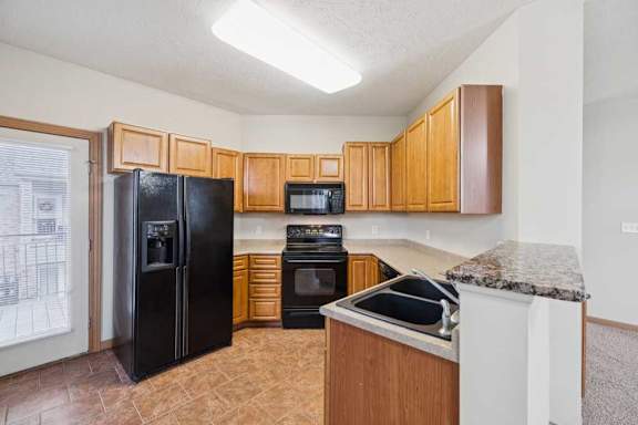 U-shaped apartment kitchen with wood cabinetry, black appliances, oven with over-the-range microwave, double-basin sink, and laminate countertops.