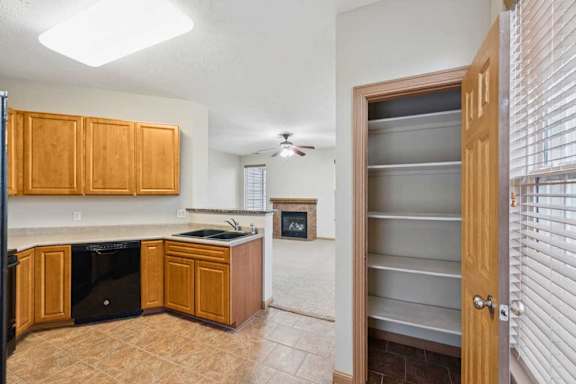 Kitchen and living area view featuring wood cabinets, double-basin sink, black dishwasher, breakfast bar, and adjacent pantry closet.