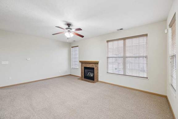 Open living area with large windows, neutral carpet, and a corner fireplace with tile surround and wood mantel for added warmth.