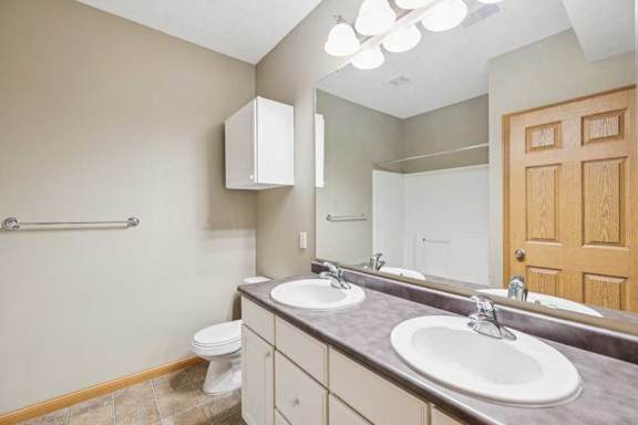 Bathroom with double-sink vanity, extended countertop, large mirror, and tub and shower combination with tile-look flooring.