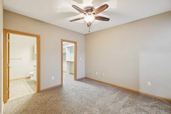 Carpeted bedroom with ceiling fan, en-suite bathroom access, and doorway to a walk-in closet.