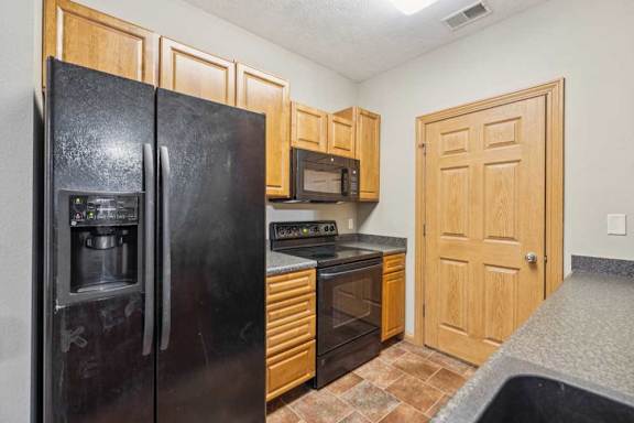 Kitchen with black refrigerator, oven, and over-the-range microwave, wood cabinetry, and a pantry closet door for extra storage.