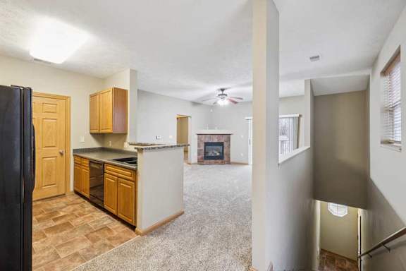 Open-concept apartment layout featuring kitchen with breakfast bar, carpeted living room, corner fireplace, and stairwell railing detail.