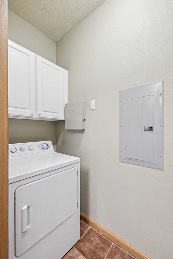 In-home laundry area with white washer and dryer, upper storage cabinets, and tile flooring.