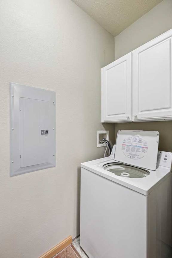 Laundry nook with top-load washer, white cabinetry, and dedicated utility hookups.