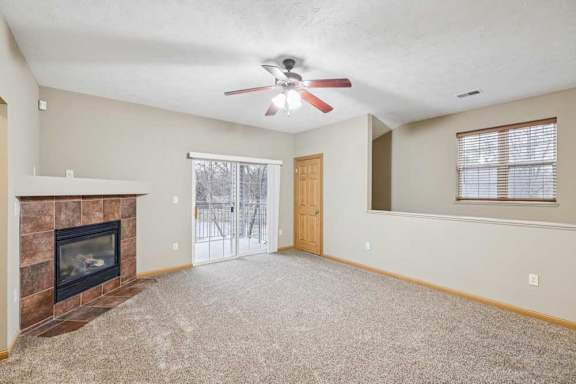 Spacious living room with ceiling fan, corner tile-surround fireplace, and sliding glass door leading to a private balcony.