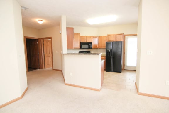 an empty living room with a kitchen with black appliances