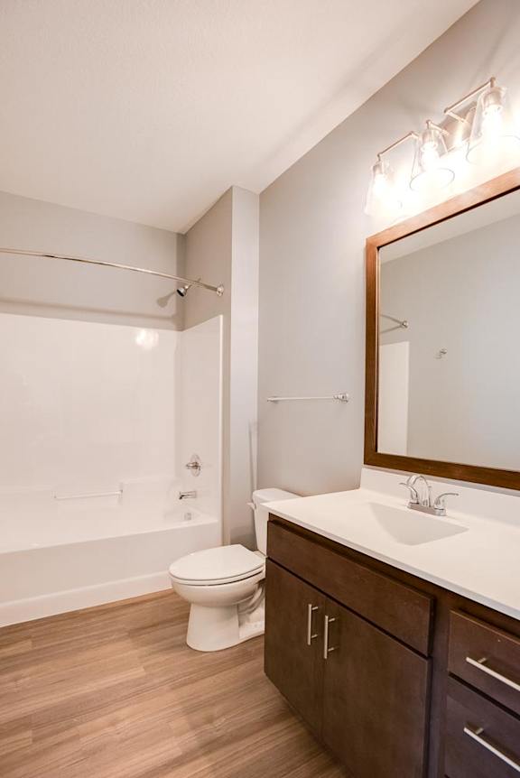 A white toilet sits in a bathroom with a wooden floor and brown cabinets.