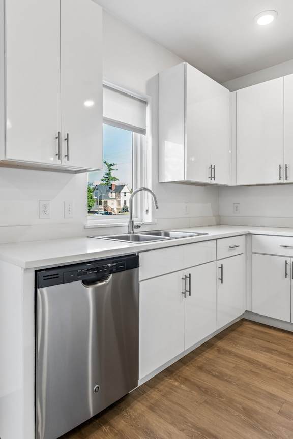 Kitchen sink beneath a sunny window, surrounded by glossy white cabinetry, generous counter space, and a stainless steel dishwasher.