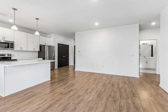 Open-concept apartment interior with a white kitchen, peninsula seating area, wood-look floors, and a bathroom visible off the living space.