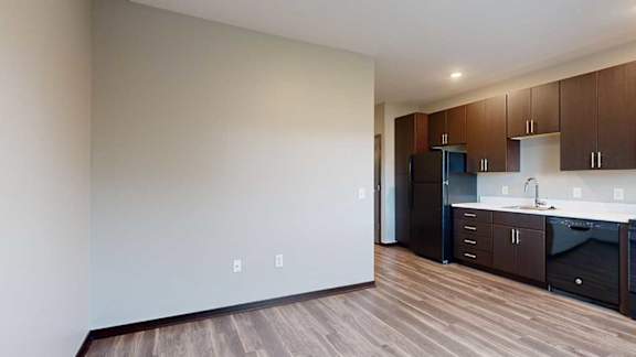 a kitchen with dark wood cabinets next to a living area with hardwood floors