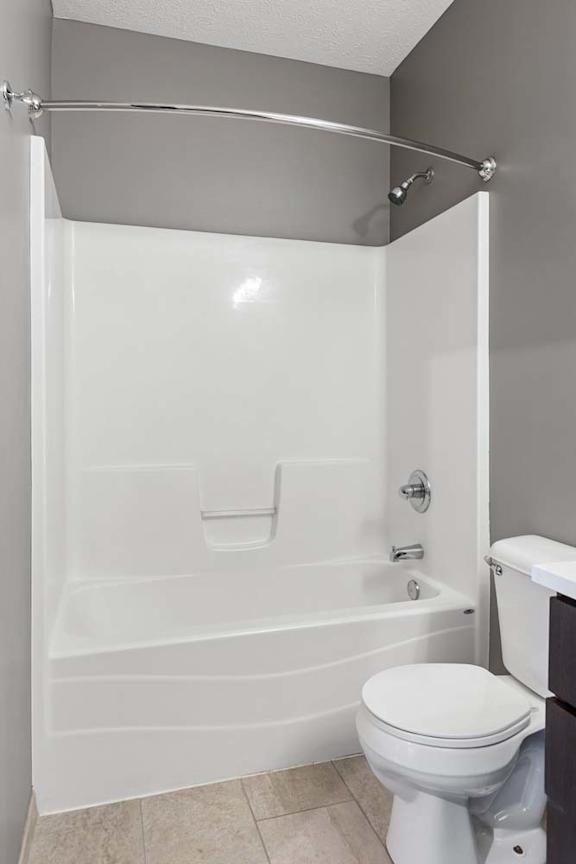 Bathroom with charcoal gray walls, a white tub and shower combination, curved curtain rod, and neutral tile flooring.