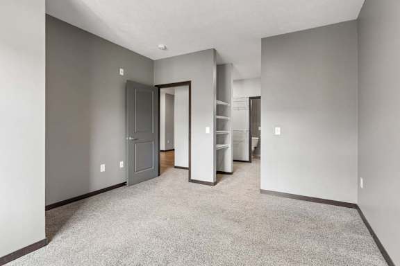 Generously sized bedroom with soft carpeting, gray walls, and an open closet area featuring built-in shelving and hanging storage.