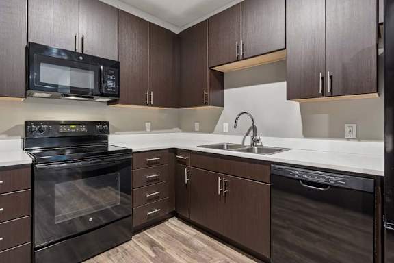 U-shaped apartment kitchen pairs dark wood cabinetry with crisp white counters, a double sink, and black appliances.