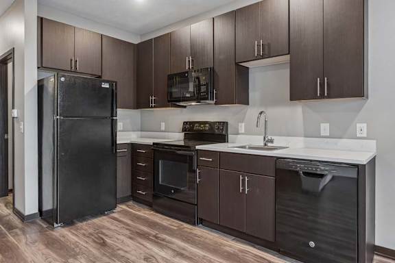 Contemporary apartment kitchen with dark wood cabinetry, black appliances, white countertops, and a functional U-shaped layout.