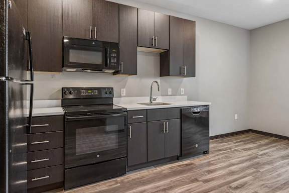 Stylish apartment kitchen with dark wood cabinetry, black appliances, white countertops, and an open dining area.